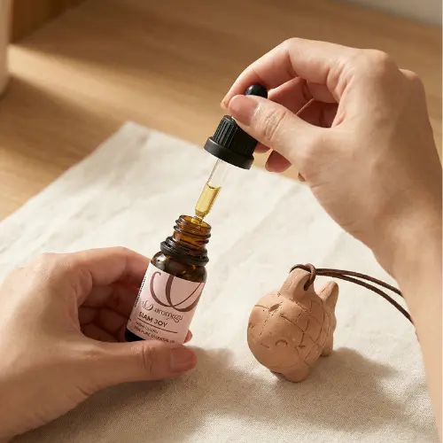 Dropping AROMAYU Siam Joy essential oil with rice paddy herb onto a wooden fish diffuser